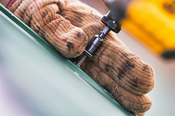 Close-up shot of a worker's gloved hands securing a metal roof screw, illustrating detailed roof repair and installation work. Close-up shot of a worker's gloved hands securing a metal roof screw, illustrating detailed roof repair and installation work.