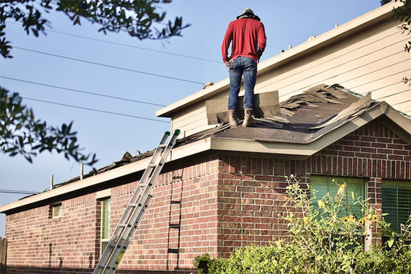 Worker inspecting a residential roof for damage, determining whether repair, patching, or replacement is needed. Worker inspecting a residential roof for damage, determining whether repair, patching, or replacement is needed.