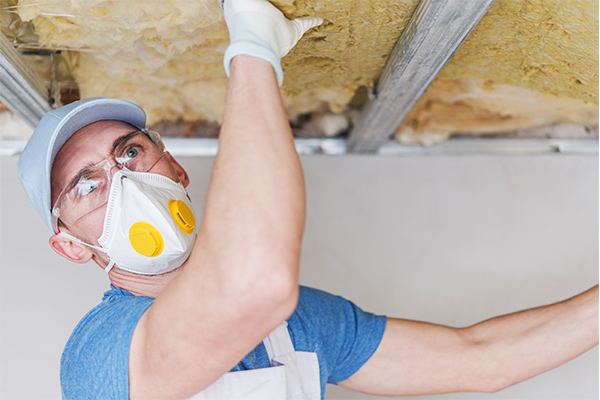 Worker installing insulation under a roof, highlighting the importance of proper insulation to prepare homes for winter weather Worker installing insulation under a roof, highlighting the importance of proper insulation to prepare homes for winter weather