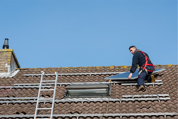 Worker installing solar panels on a tiled roof, showcasing an environmentally friendly roofing option for sustainable energy solutions. Worker installing solar panels on a tiled roof, showcasing an environmentally friendly roofing option for sustainable energy solutions.