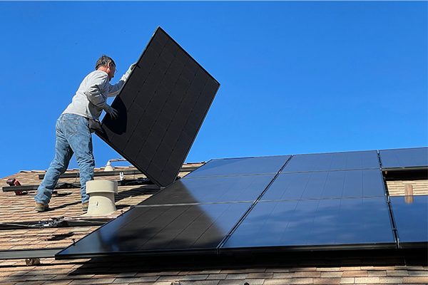 Technician installing black solar panels on a residential rooftop under a clear blue sky. Technician installing black solar panels on a residential rooftop under a clear blue sky.