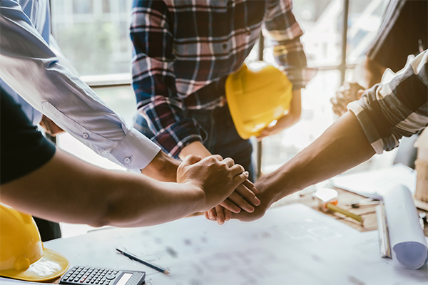 Close-up of roofing team members stacking hands over a table with blueprints and tools, symbolizing teamwork in roof replacement projects. Close-up of roofing team members stacking hands over a table with blueprints and tools, symbolizing teamwork in roof replacement projects.