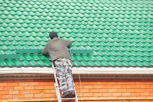 Two workers wearing protective gear are standing on scaffolding, repairing or painting the white-tiled roof of a residential building with red brick accents. Two workers wearing protective gear are standing on scaffolding, repairing or painting the white-tiled roof of a residential building with red brick accents.
