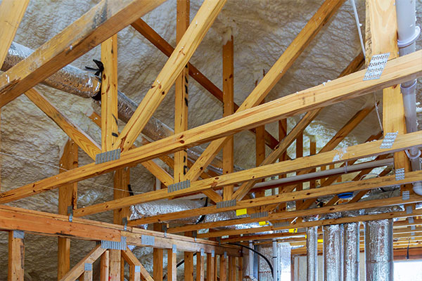 Exposed wooden trusses and spray foam insulation in a newly constructed attic, showcasing structural support and energy efficiency improvements Exposed wooden trusses and spray foam insulation in a newly constructed attic, showcasing structural support and energy efficiency improvements