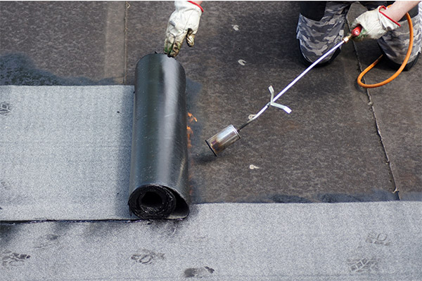 Worker installing a waterproof membrane on a flat roof using a torch-down technique, ensuring a durable and weather-resistant roofing system. Worker installing a waterproof membrane on a flat roof using a torch-down technique, ensuring a durable and weather-resistant roofing system.