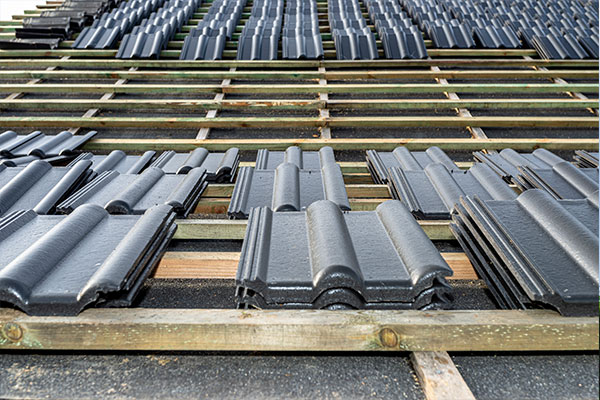 Close-up view of black roof tiles being installed on a wooden framework, showcasing the early stages of a roof installation process. Close-up view of black roof tiles being installed on a wooden framework, showcasing the early stages of a roof installation process.