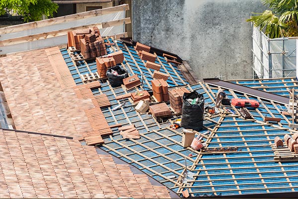 Aerial view of a residential roof under renovation with wooden framing, clay tiles, and roofing materials scattered on top. The image highlights the roof construction process and the importance of proper installation for durability and longevity. Aerial view of a residential roof under renovation with wooden framing, clay tiles, and roofing materials scattered on top. The image highlights the roof construction process and the importance of proper installation for durability and longevity.