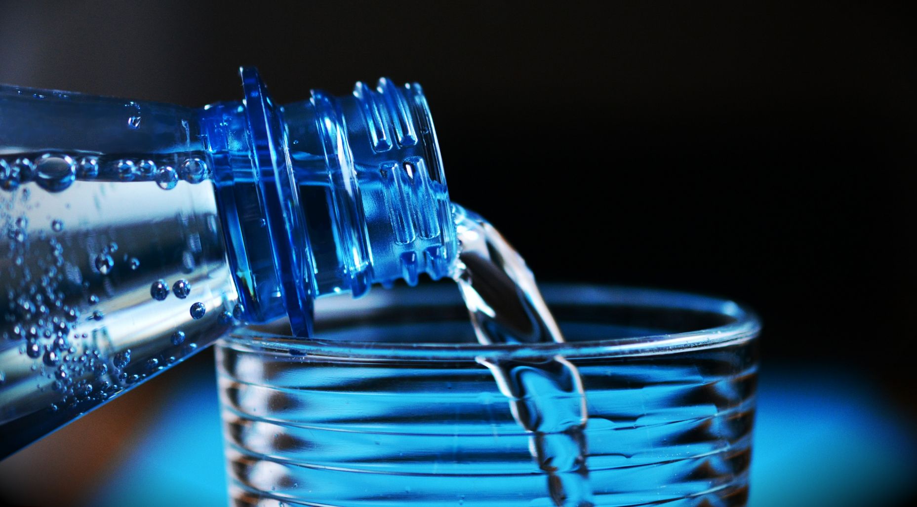 Water bottle pouring into a glass cup.