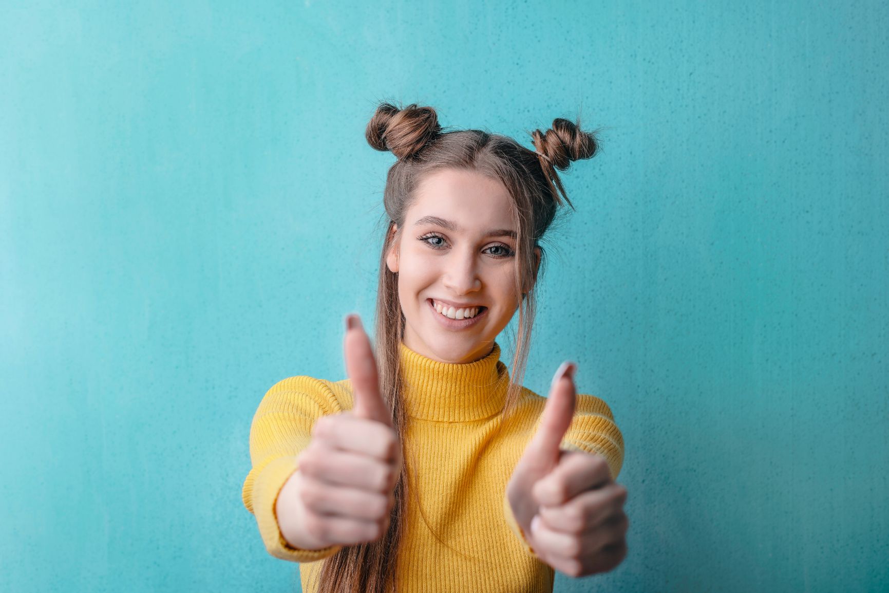 Woman wearing yellow in front of blue background giving two thumbs up