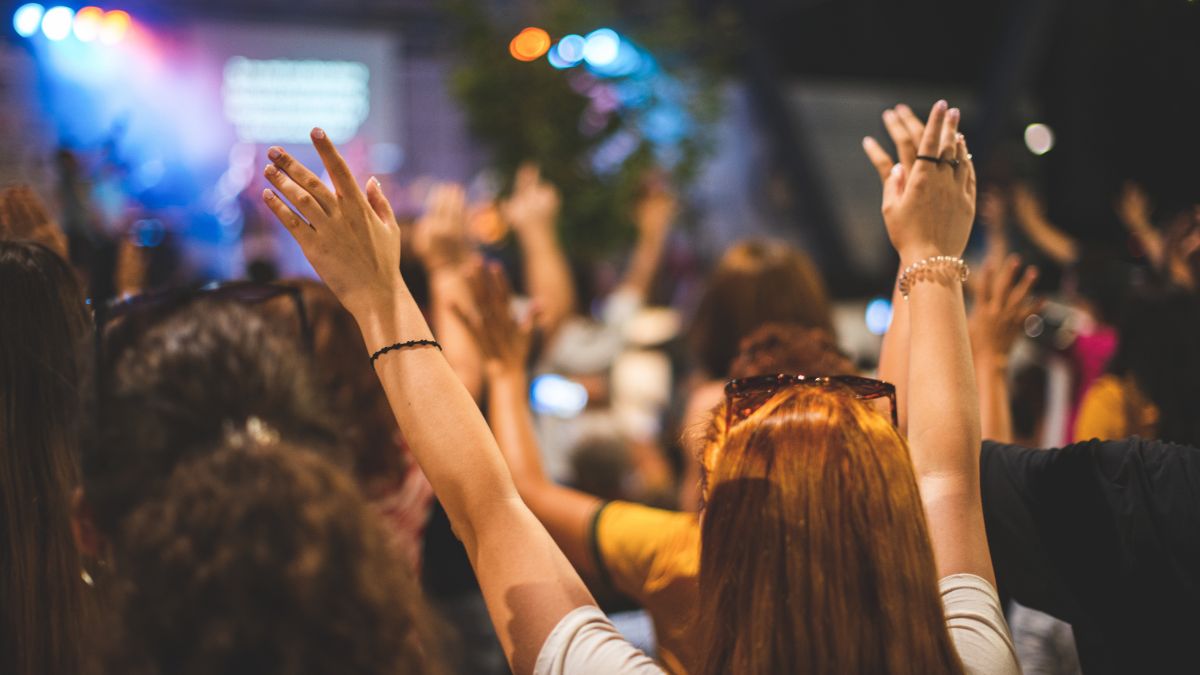 A large group of church members with arms raised in worship facing stage with lights.