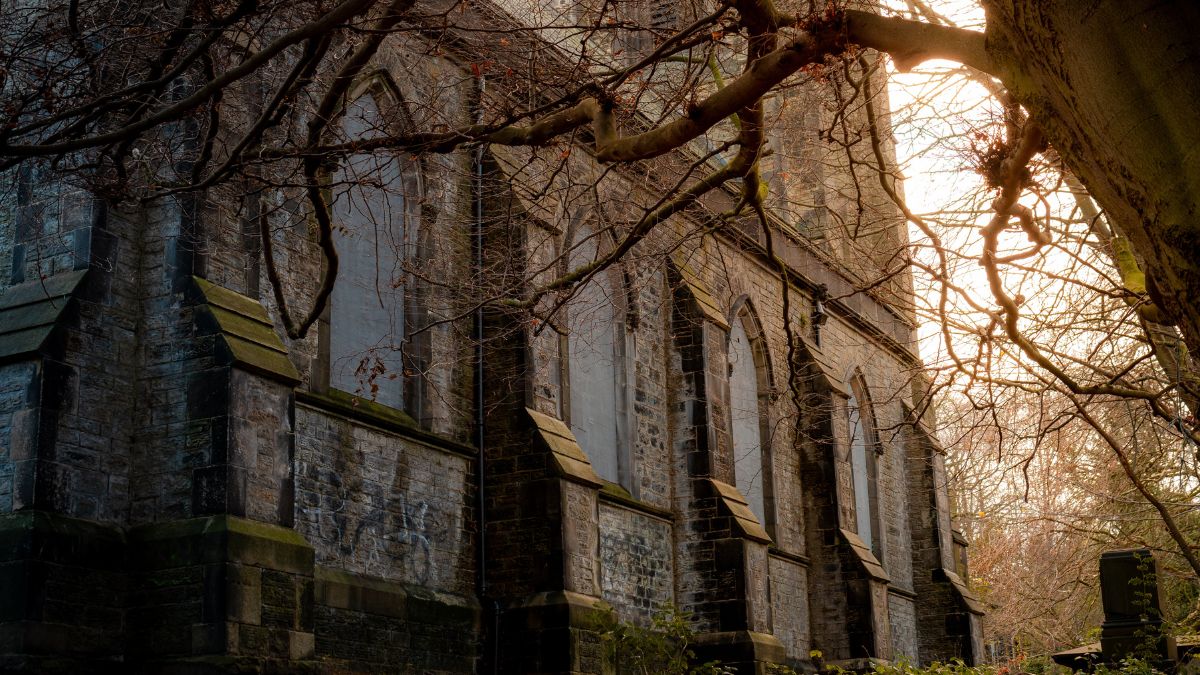 An abandoned stone church with boarded windows in the forest during winter. 