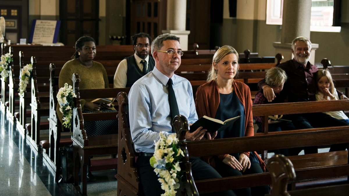 A couple holding a prayer book during a church service with other worshippers behind them.