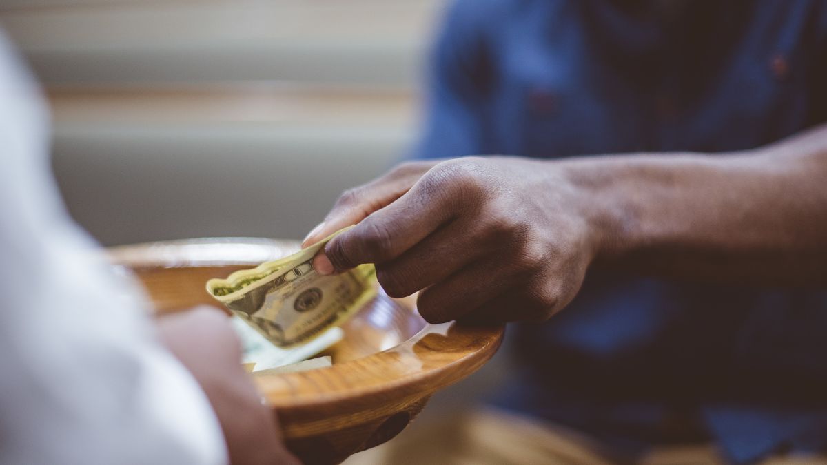 Close-up of man putting money in church donation plate.