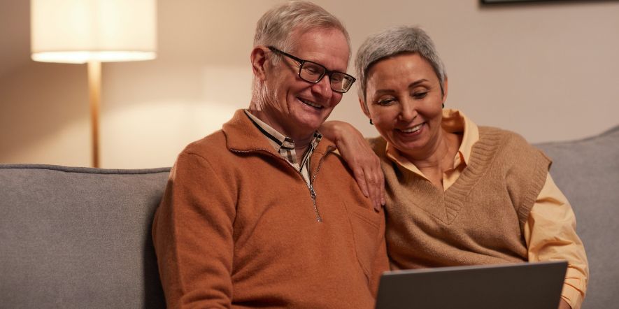 An older man and woman sitting on a sofa and smiling at a laptop as they take a church survey.