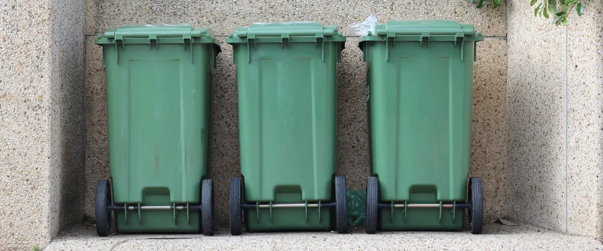 Three green curbside trash bins lined up in a concrete alcove