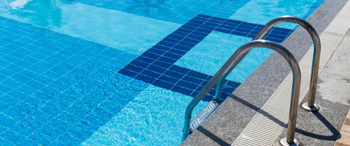 Modern swimming pool with stainless steel ladder and blue mosaic tiles