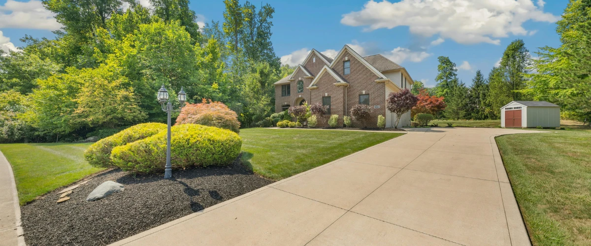 Beautifully maintained concrete driveway with lush landscaping leading to a modern brick home." Beautifully maintained concrete driveway with lush landscaping leading to a modern brick home."
