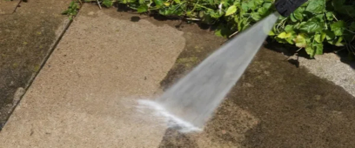 High-pressure water cleaning a concrete driveway surface outdoors