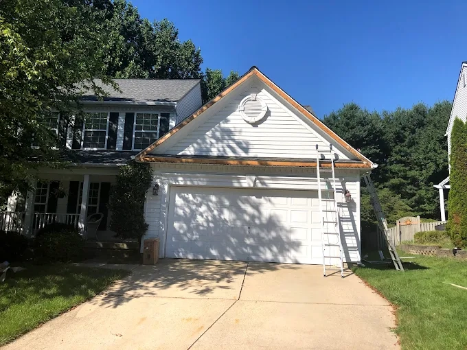 a house undergoing remodeling with a ladder against the roof and a new section of siding being installed.
