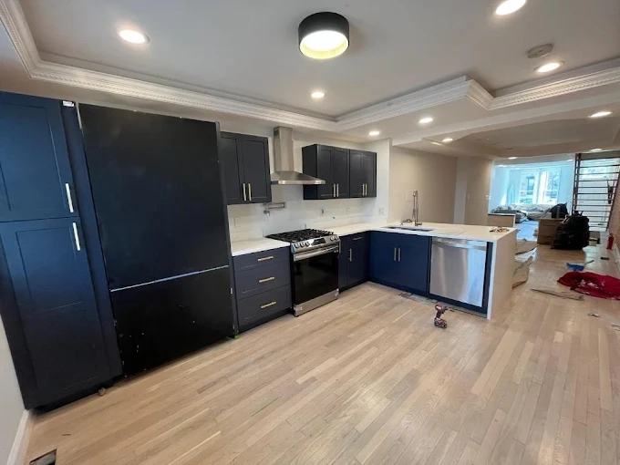 a remodeled kitchen with modern navy cabinets, stainless steel appliances, and new hardwood flooring.