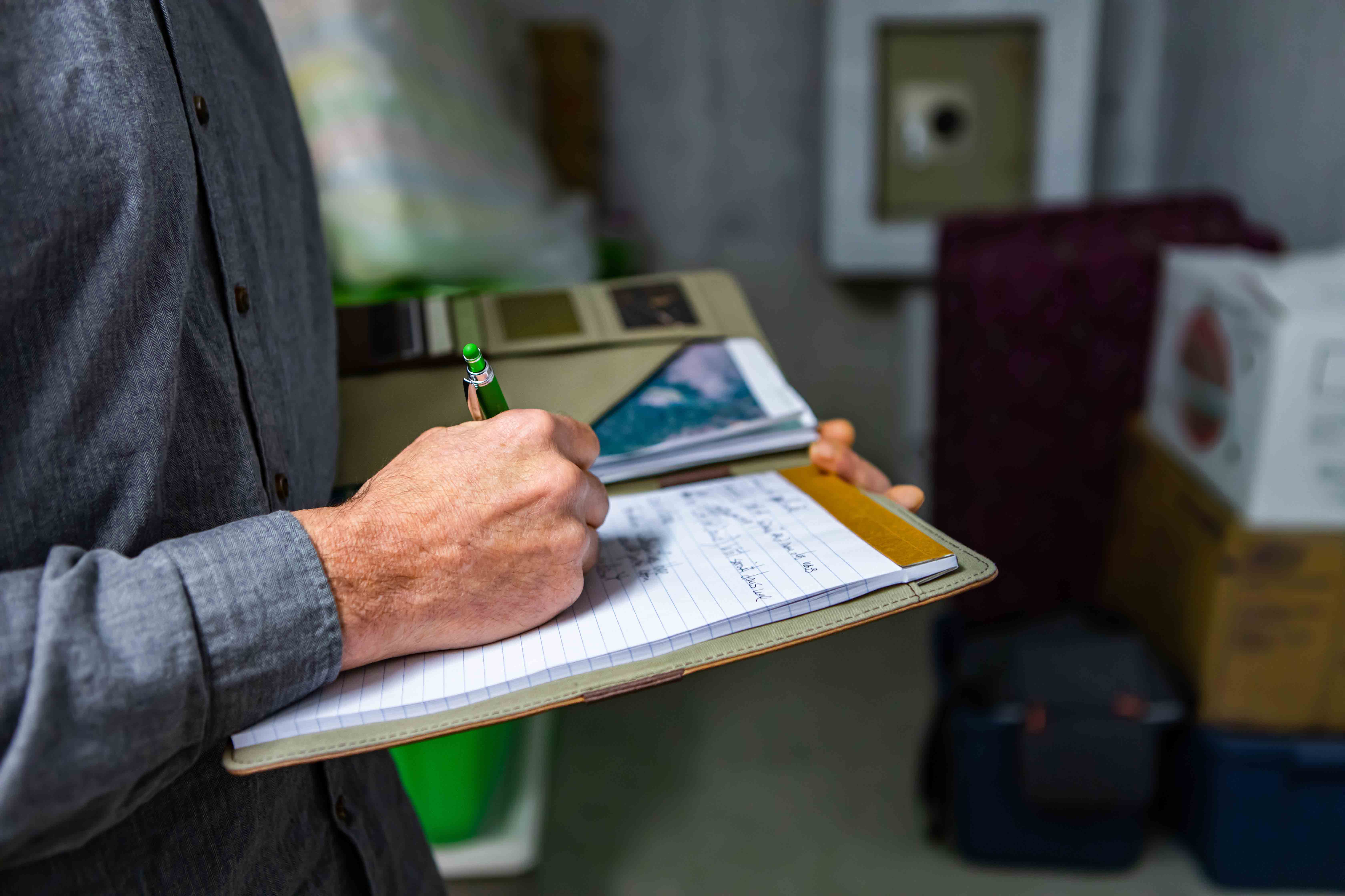 A man writing on a clipboard in a storage room.