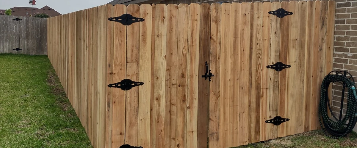 Wooden privacy fence with black metal hinges and gate beside a brick wall. Wooden privacy fence with black metal hinges and gate beside a brick wall.