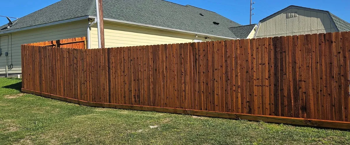 Long stained wooden privacy fence running along a residential side yard Long stained wooden privacy fence running along a residential side yard