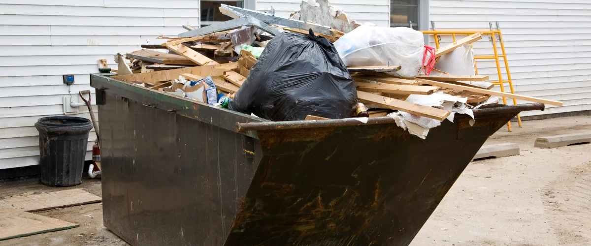 Construction debris dumpster filled with wood, scrap materials, and trash outside a building.
