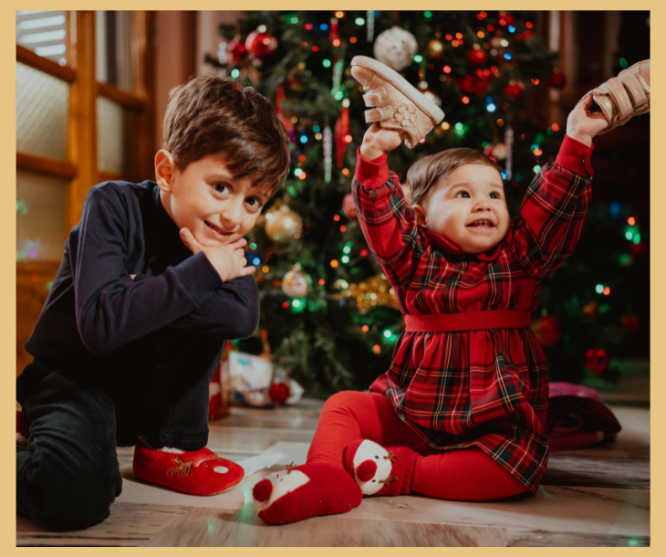 A baby and toddler sat in front of a beautiful Christmas tree
