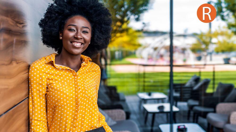 A PICTURE OF A SMILING WOMAN LEANING AANGINST A VIBRANT WALL