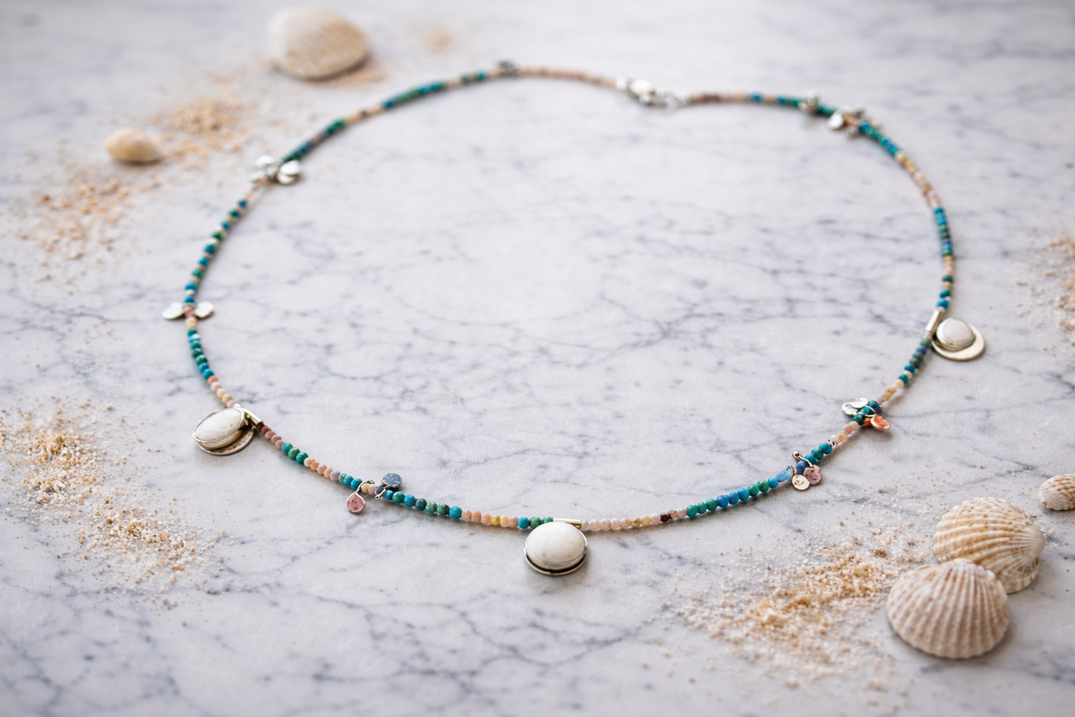 Handmade silver beaded necklace inspired by ancient Greek island jewelry, featuring turquoise beads, pink opals, and white pebble charms arranged asymmetrically on a marble surface Handmade silver beaded necklace inspired by ancient Greek island jewelry, featuring turquoise beads, pink opals, and white pebble charms arranged asymmetrically on a marble surface