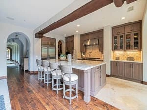 A spacious kitchen with painting wooden cabinets, a large central island with stools, and an open archway leading to another room.