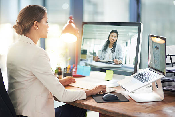 Two doctors are discussing a case on a laptop screen in a virtual meeting, with other attendees watching remotely.