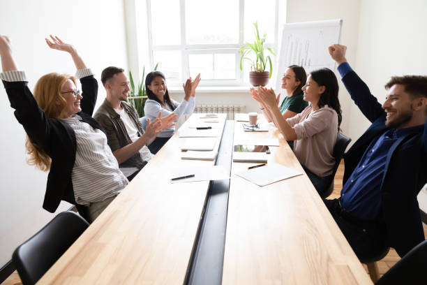 A group of diverse co-workers whooping and high-fiving at the office.