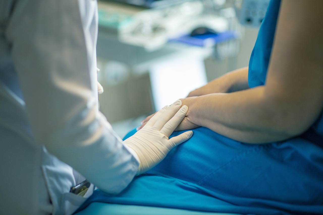 Doctor wearing gloves gently placing a hand on a patient's hand during a medical visit.
