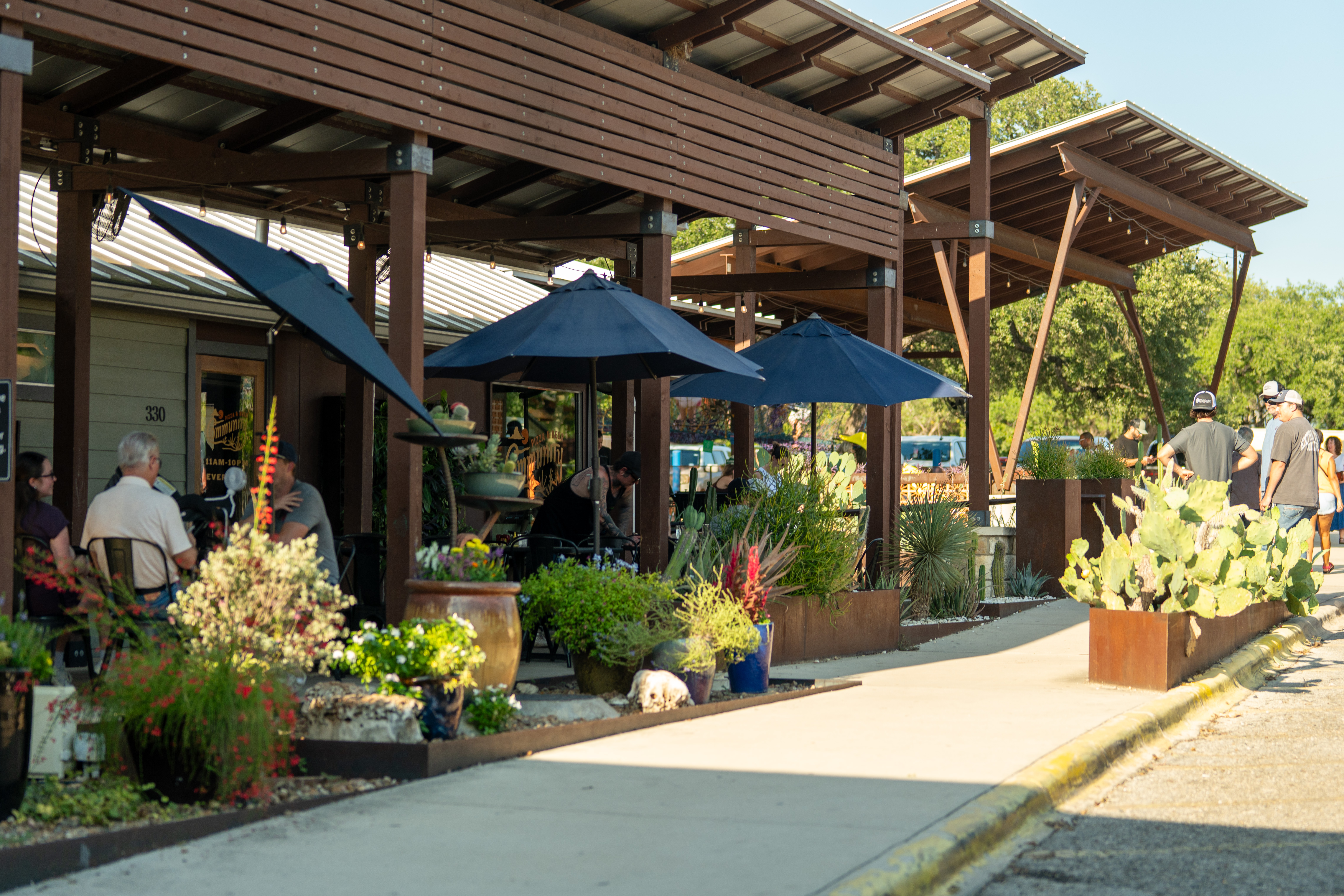 Outdoor patio at Community Pizza & Beer Garden in Wimberley, TX, with diners enjoying wood-fired pizza under umbrellas and Hill Country sunshine. Outdoor patio at Community Pizza & Beer Garden in Wimberley, TX, with diners enjoying wood-fired pizza under umbrellas and Hill Country sunshine.