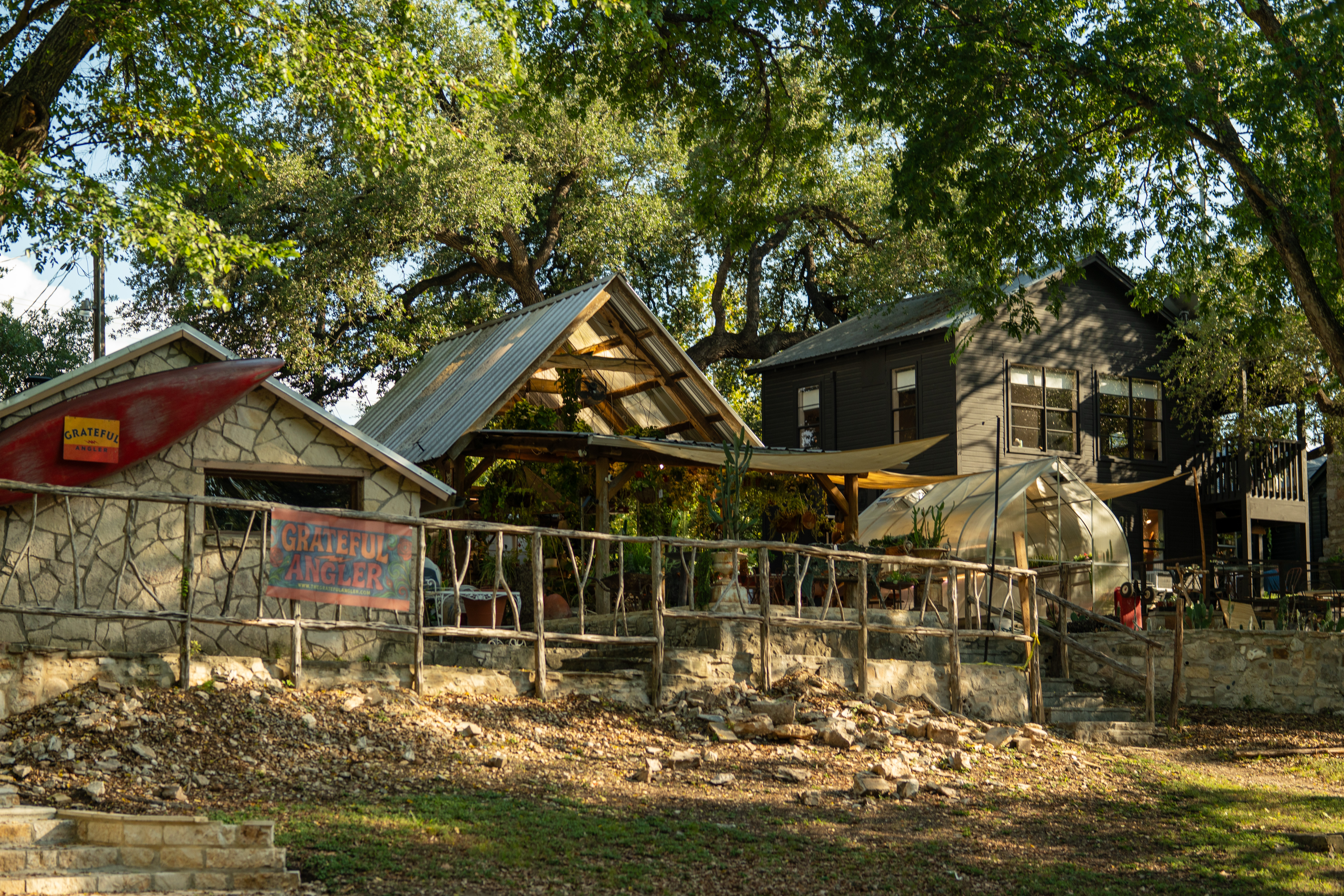 Shops along Cypress Creek in Wimberley, TX, including The Grateful Angler fly-fishing shop and local artisan spaces under the shade of oak trees. Shops along Cypress Creek in Wimberley, TX, including The Grateful Angler fly-fishing shop and local artisan spaces under the shade of oak trees.