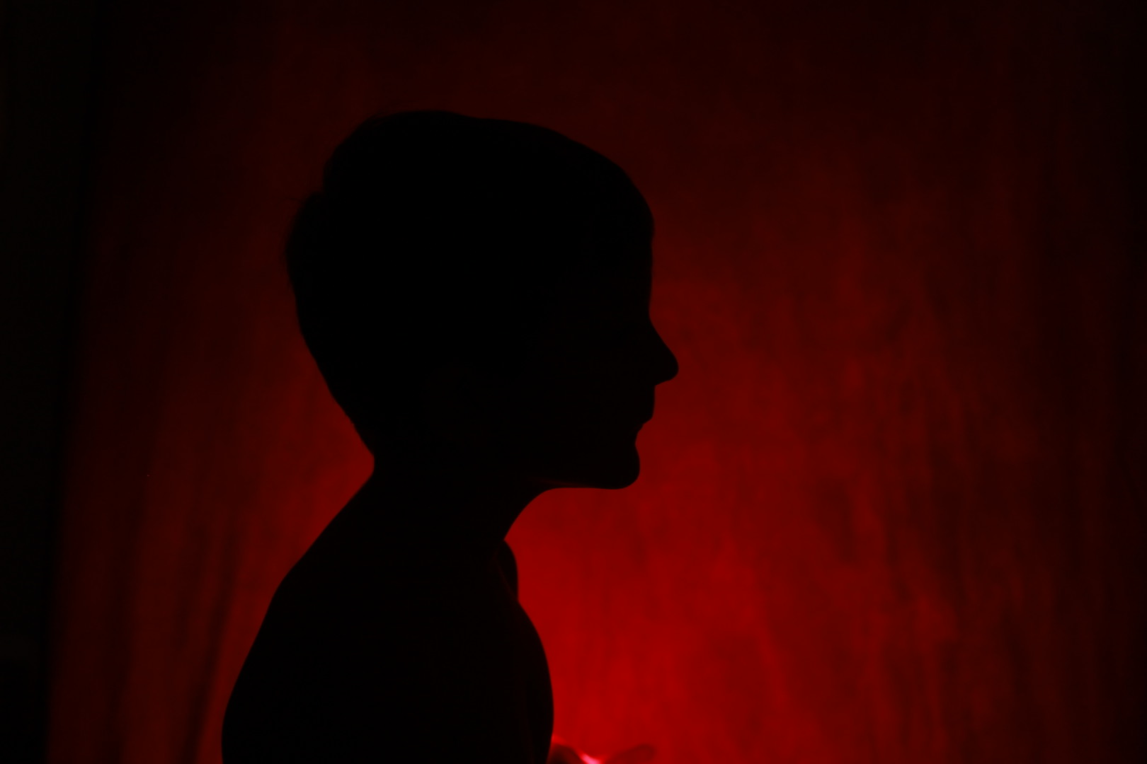 Silhouette of a child’s profile illuminated by dramatic red lighting, showcasing controlled indoor lighting techniques by Gilbert family photographer Andria May Photography.