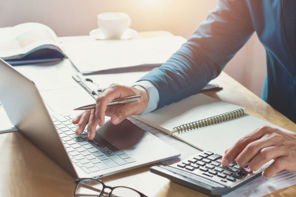 Person working on a laptop and calculator with notes Person working on a laptop and calculator with notes
