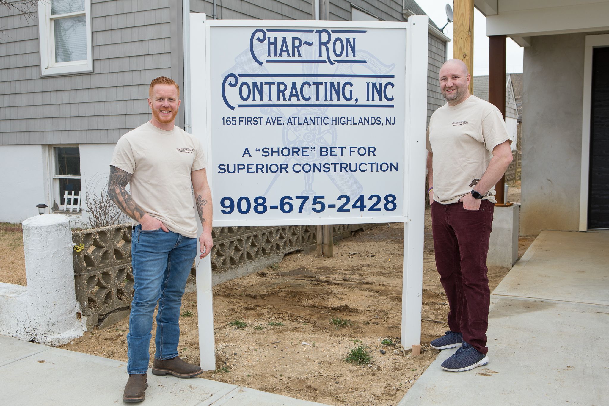 Charlie and Bill standing in front of a sign that has all of Char-Ron's information on it 