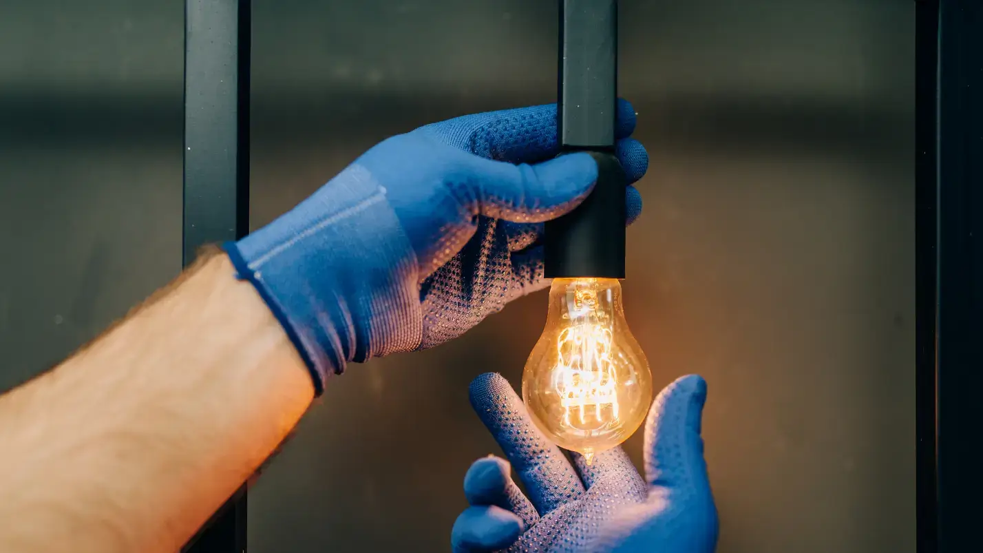 A person wearing blue gloves holds a light bulb, ready to install or replace it. A person wearing blue gloves holds a light bulb, ready to install or replace it.