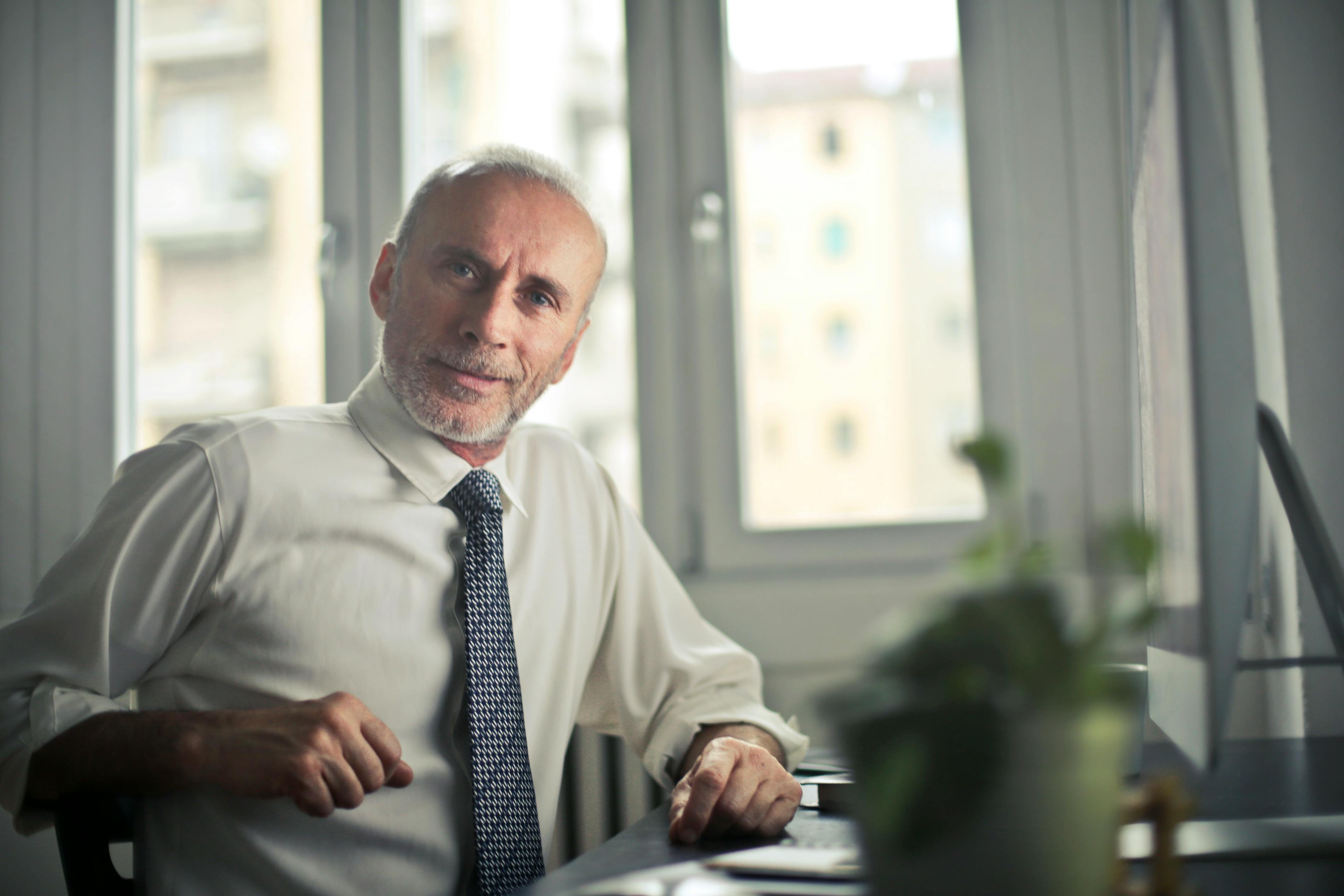 A man wearing a shirt and tie is positioned at a desk, concentrating on his work in a business-like atmosphere. A man wearing a shirt and tie is positioned at a desk, concentrating on his work in a business-like atmosphere.