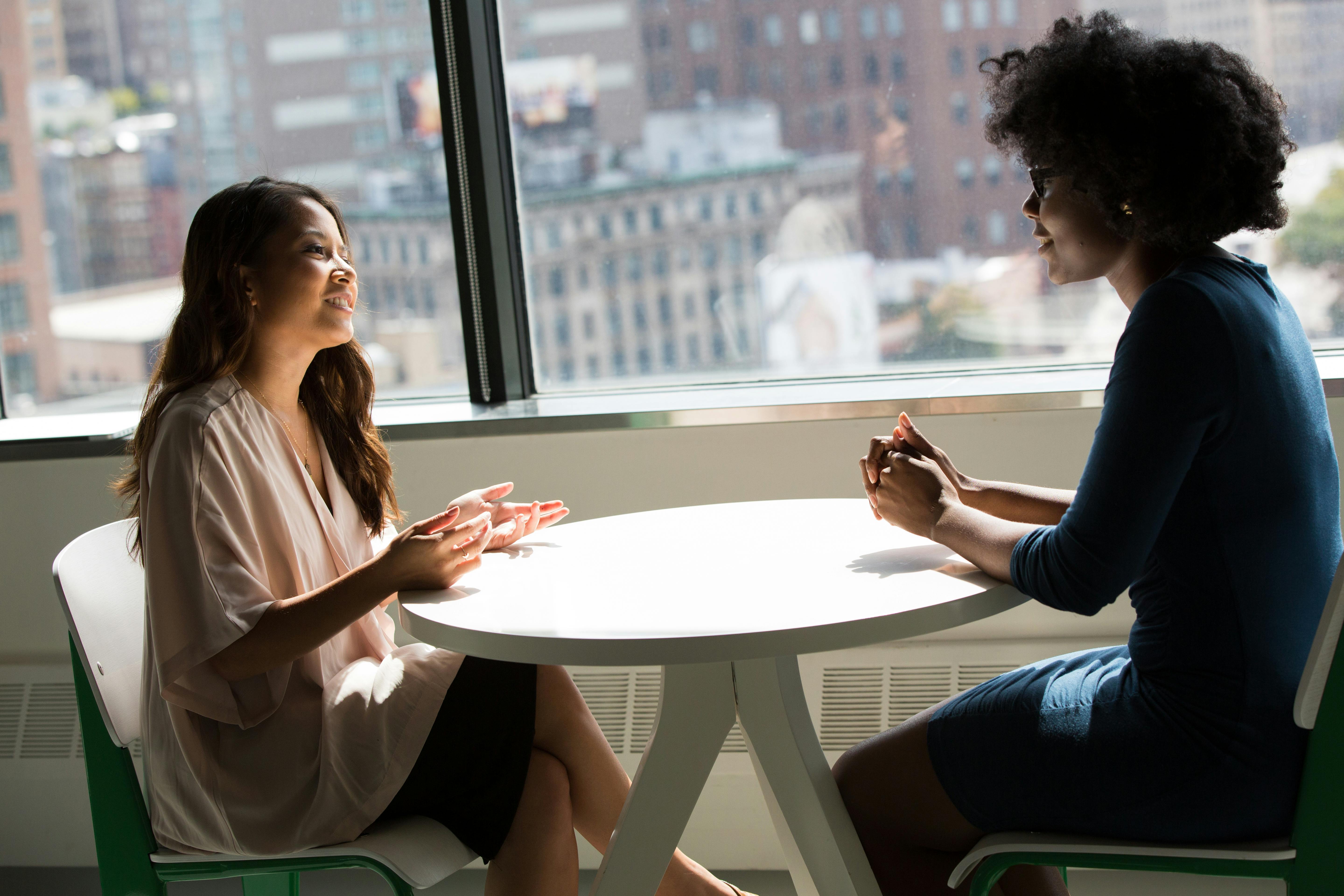 Two women engaged in conversation while sitting at a table, sharing ideas and laughter in a cozy setting.