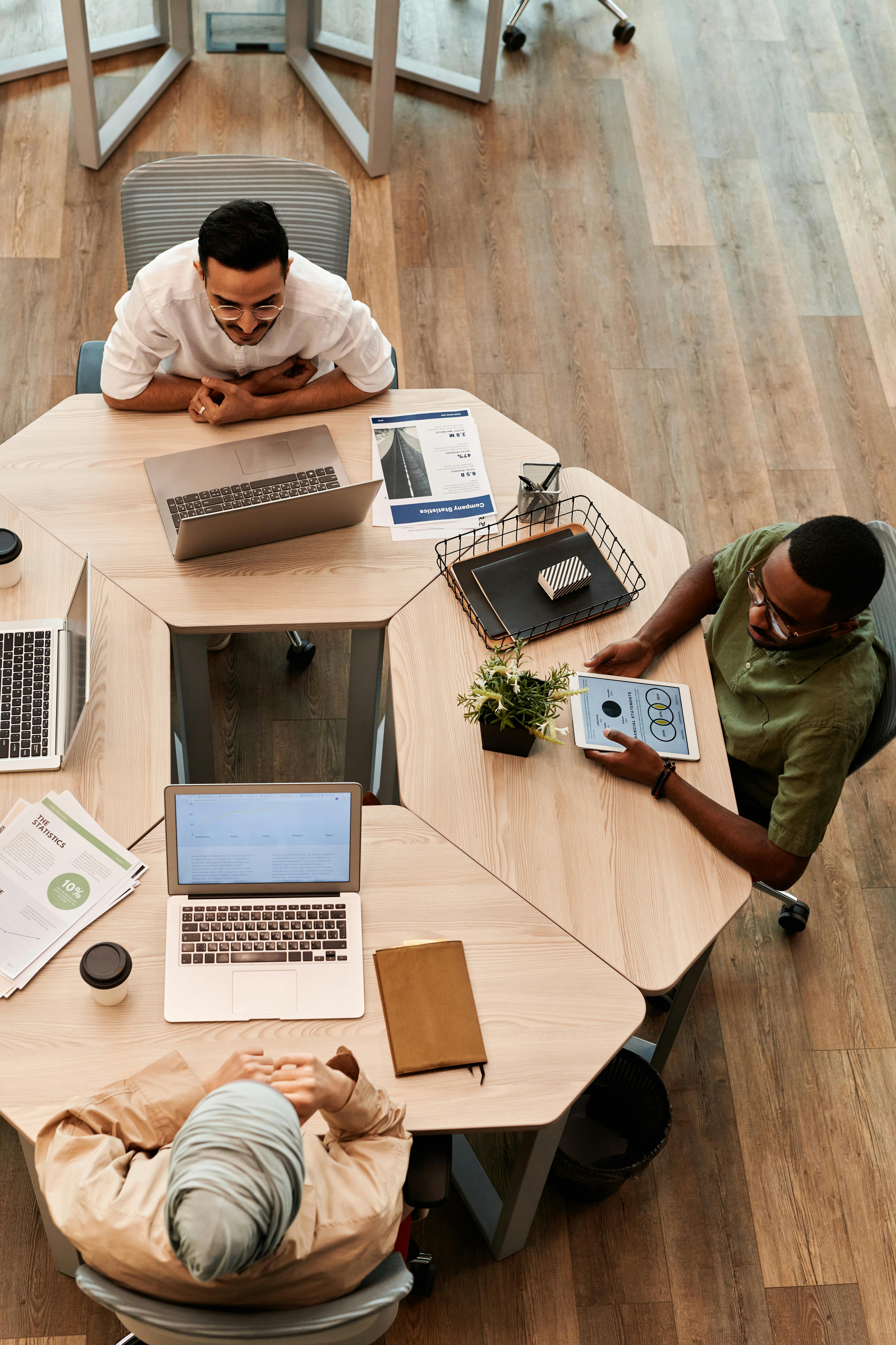 A group of four people around a table, focused on their laptops, likely working together on a project. A group of four people around a table, focused on their laptops, likely working together on a project.