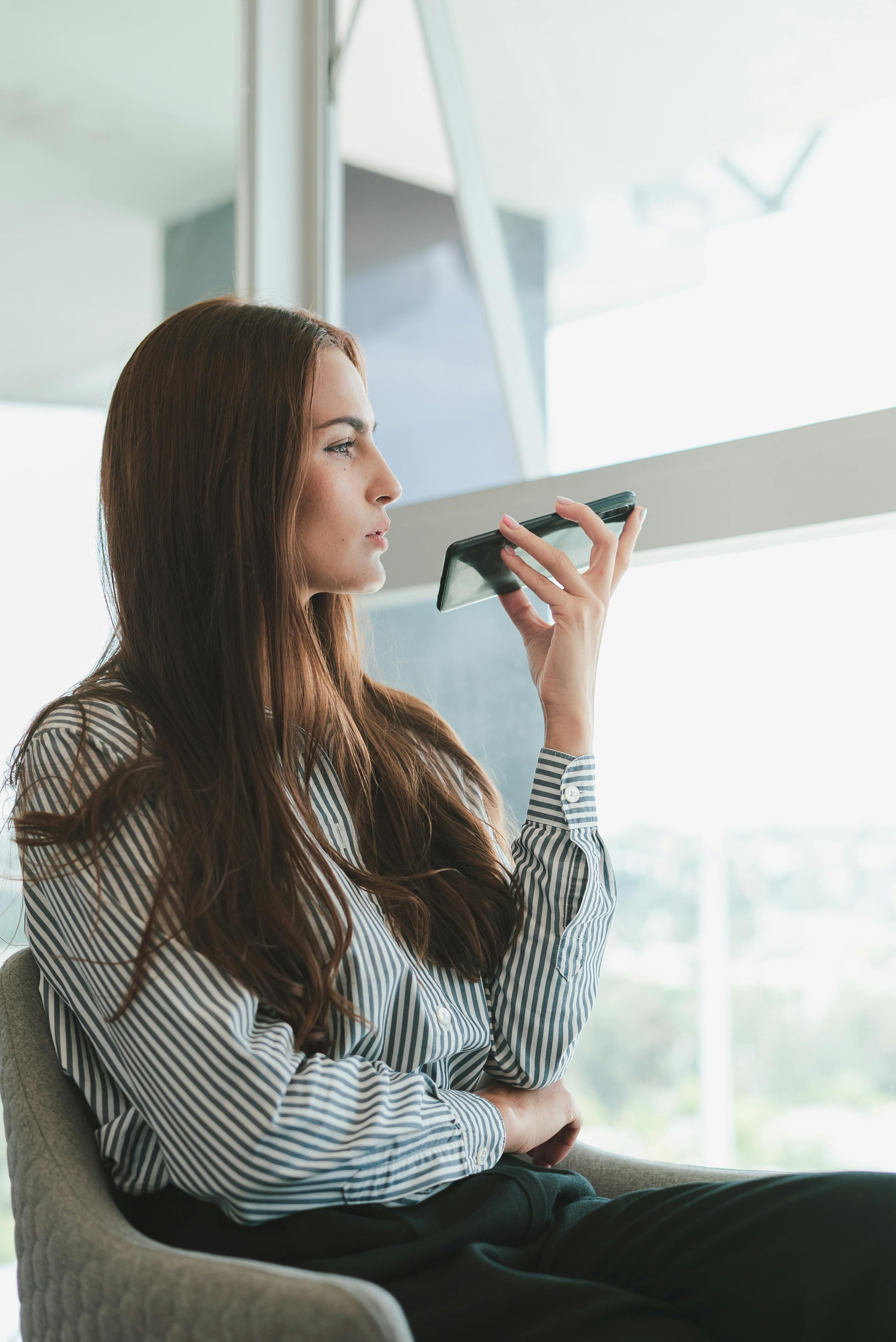A woman in a chair, holding a cell phone, seemingly absorbed in her conversation or activity on the device. A woman in a chair, holding a cell phone, seemingly absorbed in her conversation or activity on the device.