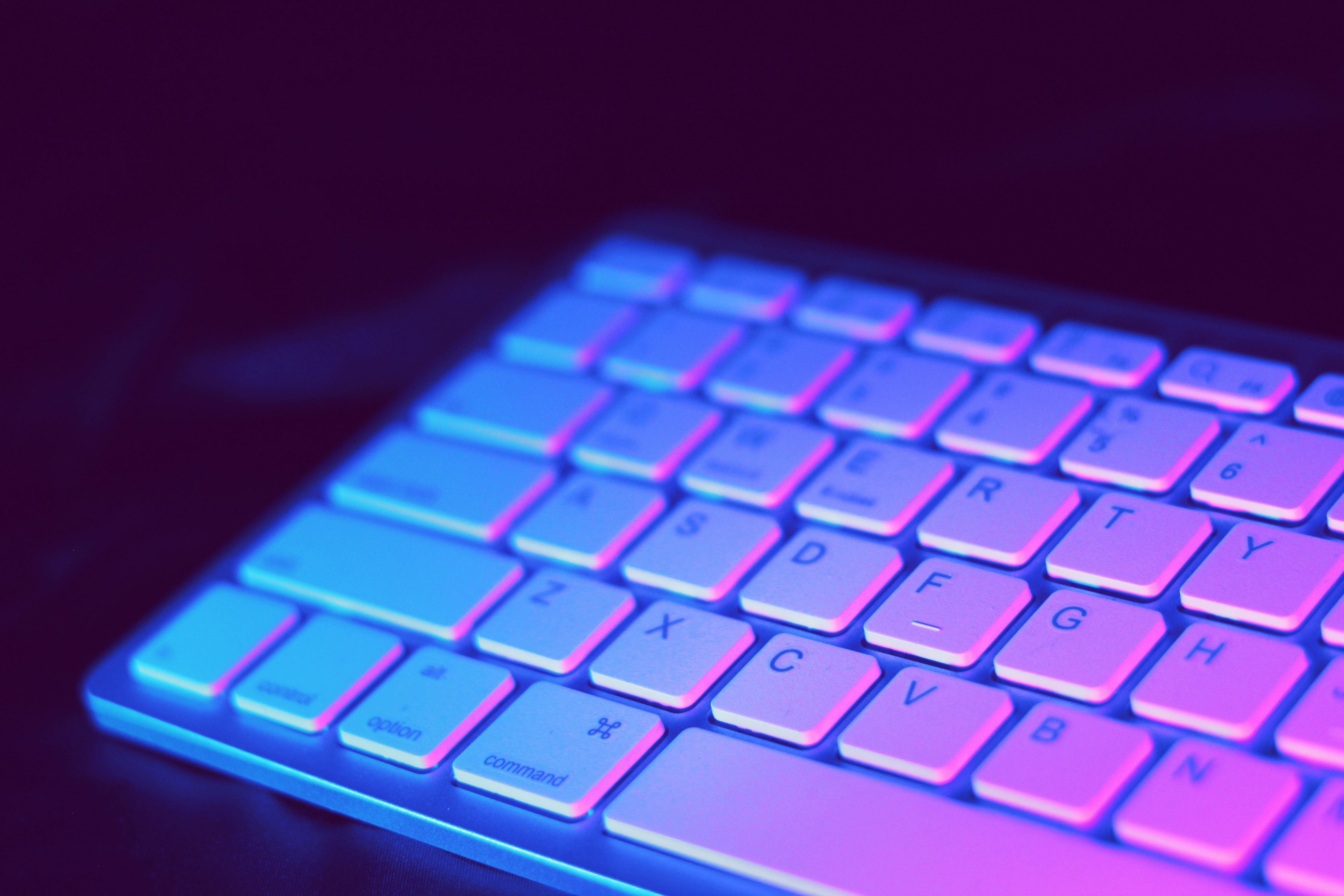 A close-up of a keyboard illuminated with vibrant purple and blue lights, creating a dynamic and colorful glow. A close-up of a keyboard illuminated with vibrant purple and blue lights, creating a dynamic and colorful glow.