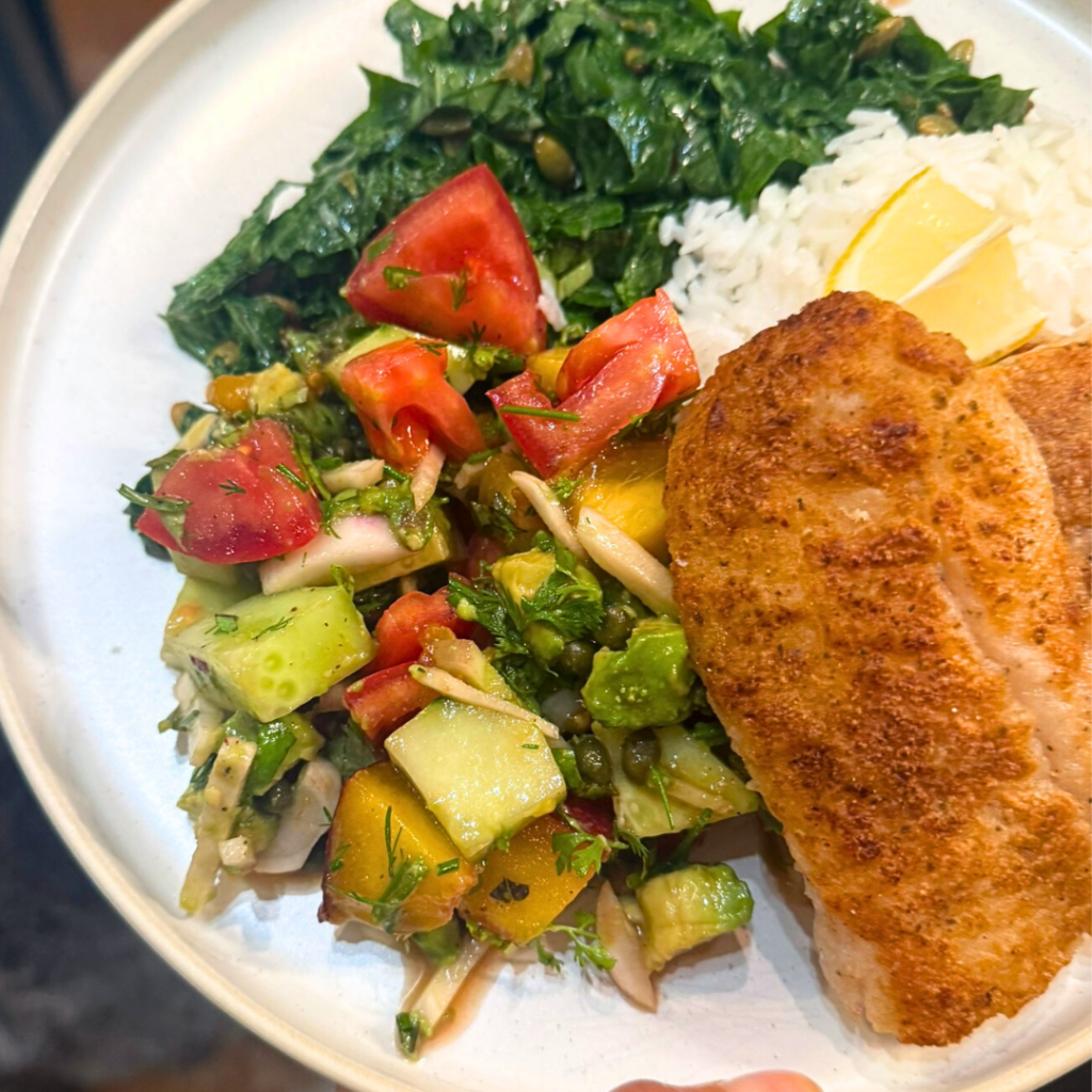Plate of summer salad with peach and tomatoes, rice, greens, and grilled fish