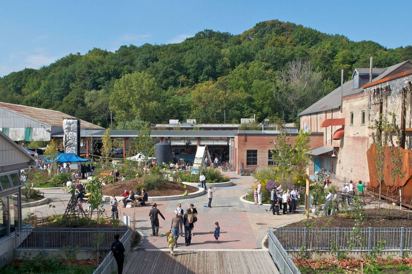 Evergreen Brick Works Toronto yard and patio with visitors exploring the restored historic brick buildings, community gardens, and event spaces surrounded by Don Valley forest hills