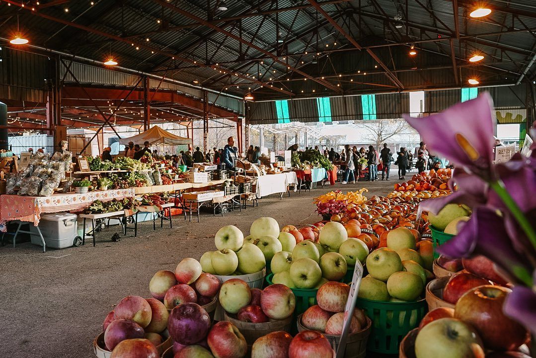Here's SEO-optimized alt text for this image: "Evergreen Brick Works Saturday farmers market Toronto featuring fresh local apples, seasonal produce, and vendors in the historic industrial pavilion with string lights and exposed steel beams