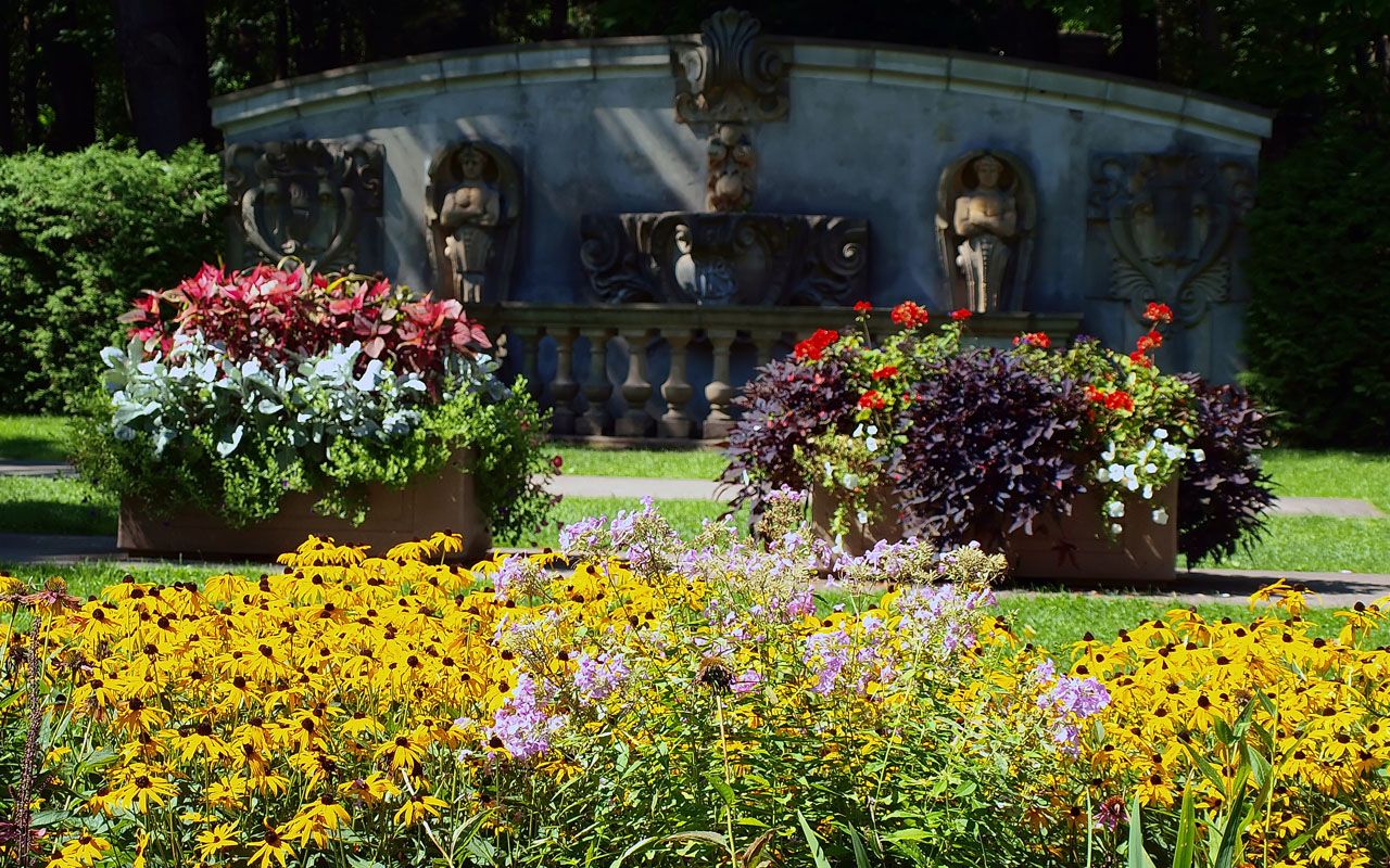 Guild Park & Gardens ornate stone monument with classical carved figures surrounded by colorful summer flower beds including black-eyed susans and purple asters in Scarborough Toronto. Image courtesy: City of Toronto